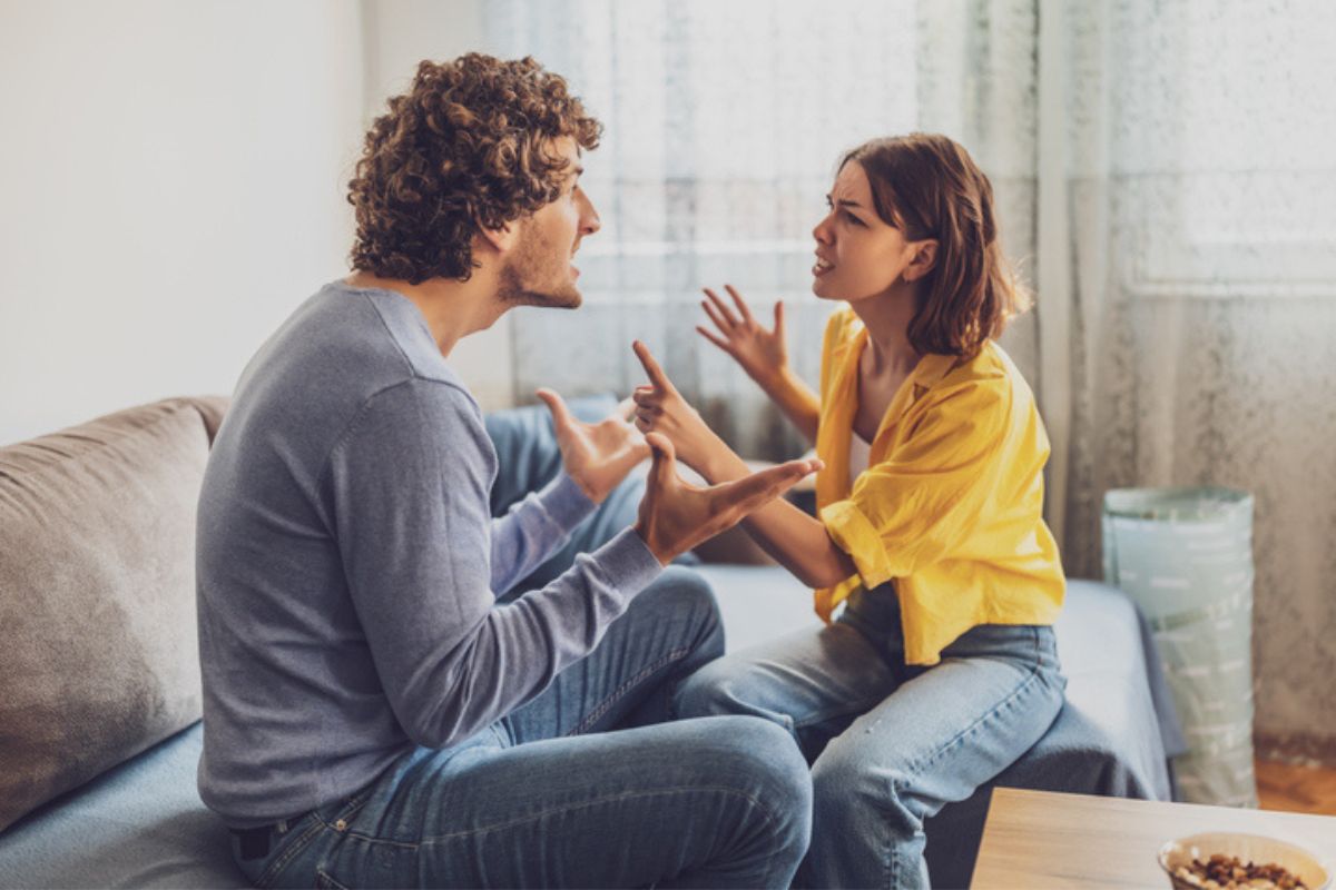 Imagem colorida de casal brigando sentados no sofá da sala