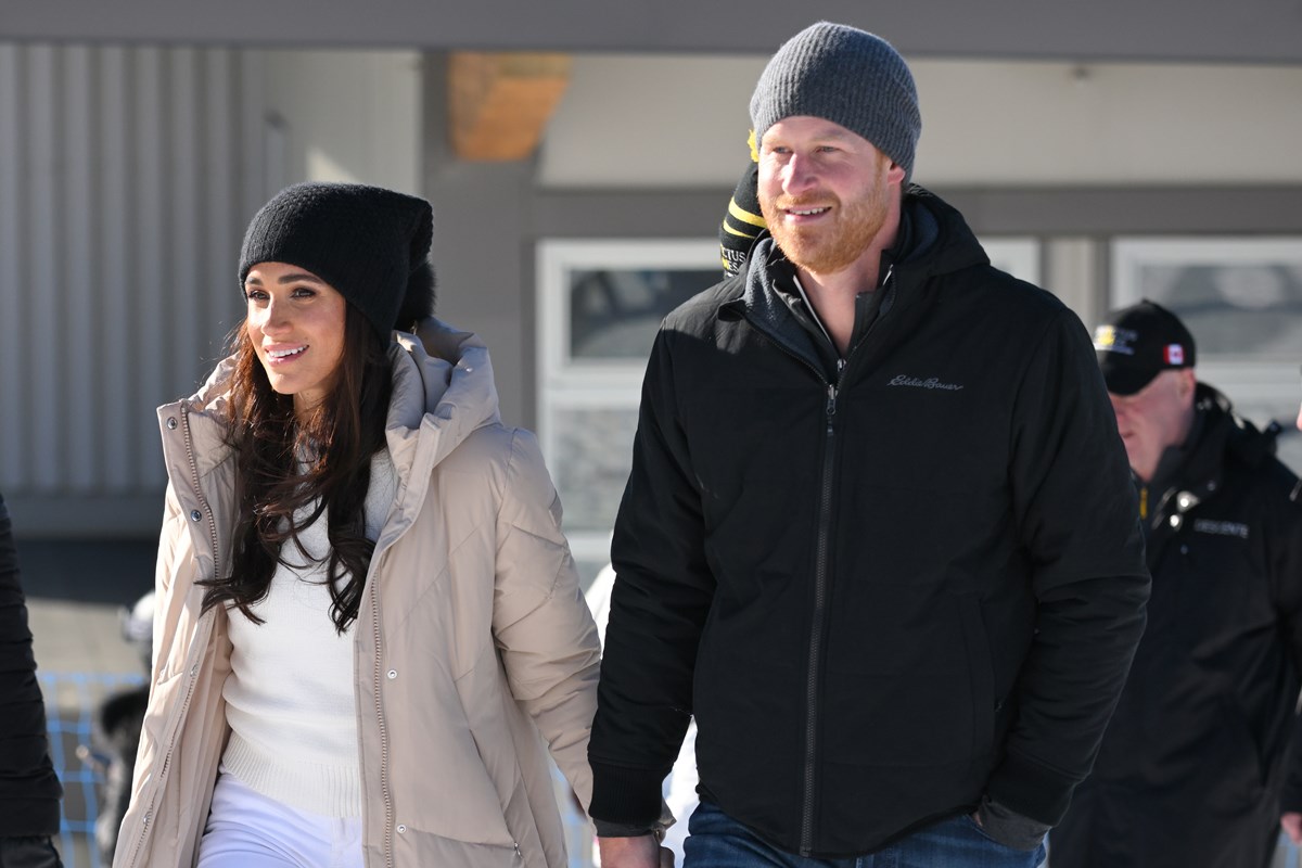 Foto colorida de mulher com touca e roupa de frio de mãos dadas com homem ruivo que usa roupas pretas - Metrópoles