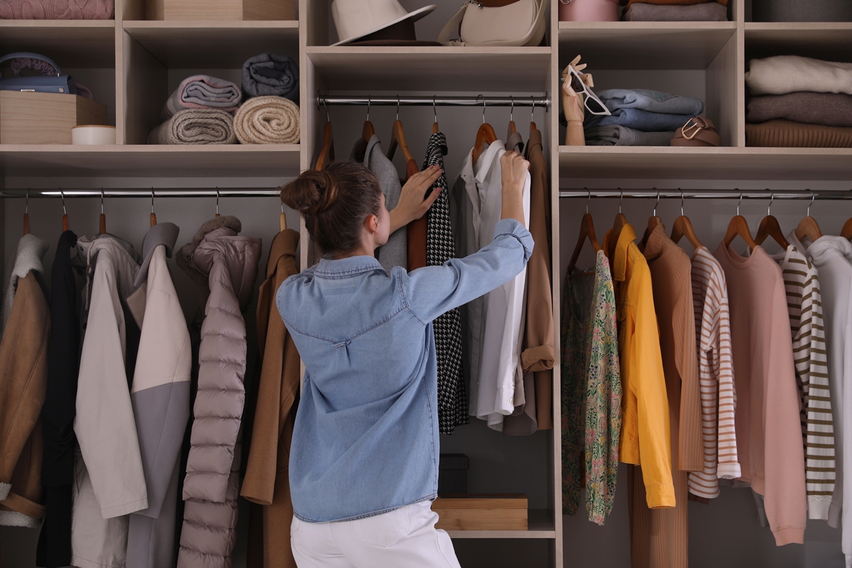 Foto colorida - Mulher pendurando blusa no guarda-roupa