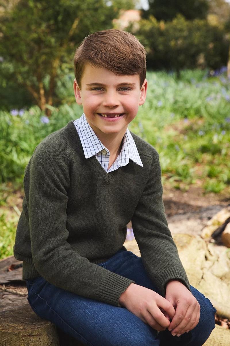 Foto colorida de menino sentado em arbusto. Ele está sorrindo - Metrópoles